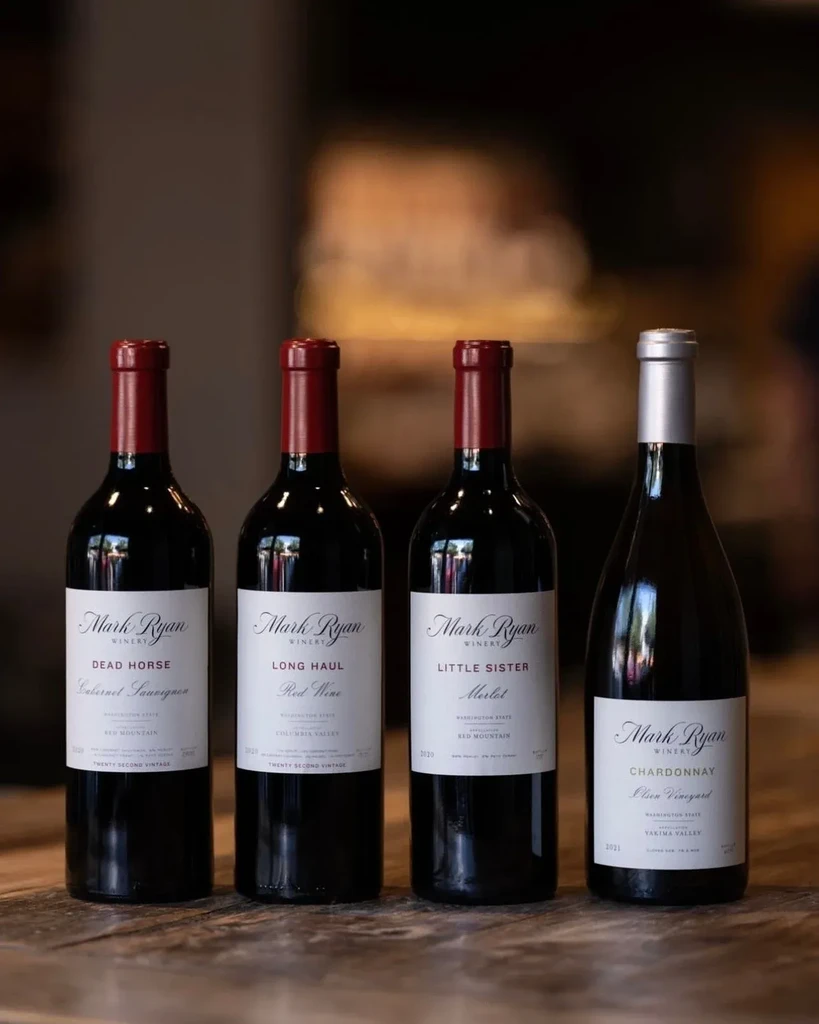 Three red and one white Mark Ryan Winery bottles on wood.