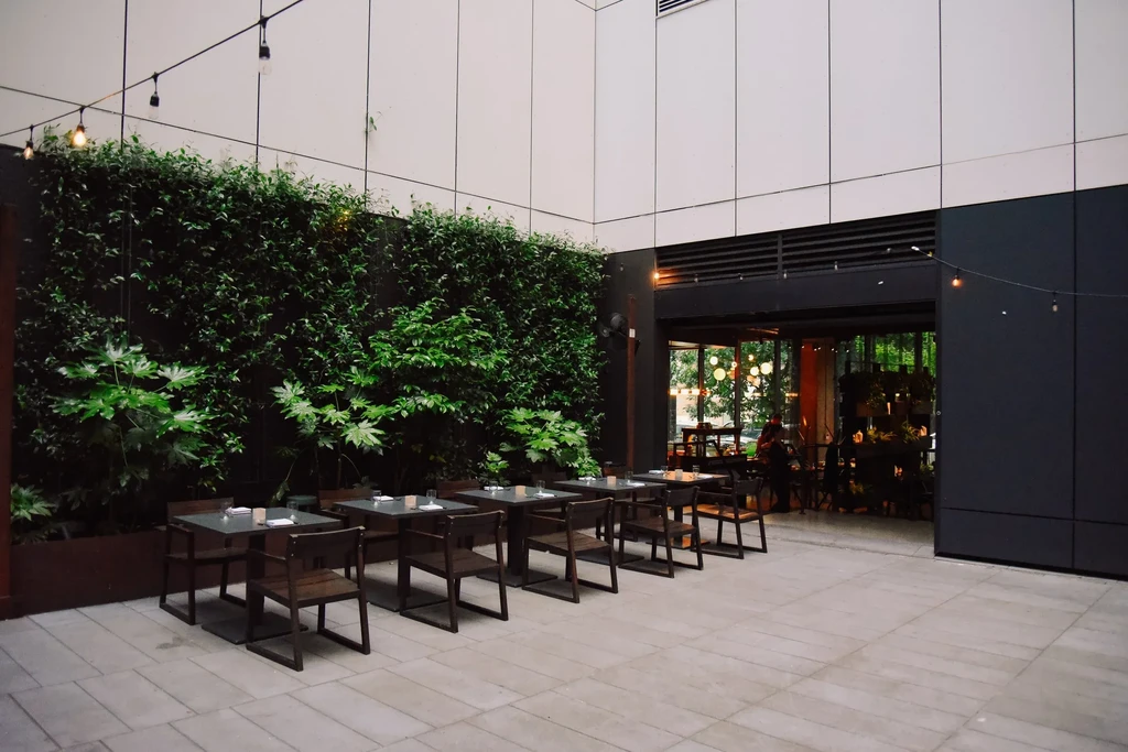 Modern restaurant patio with green living wall, string lights, and dining tables.