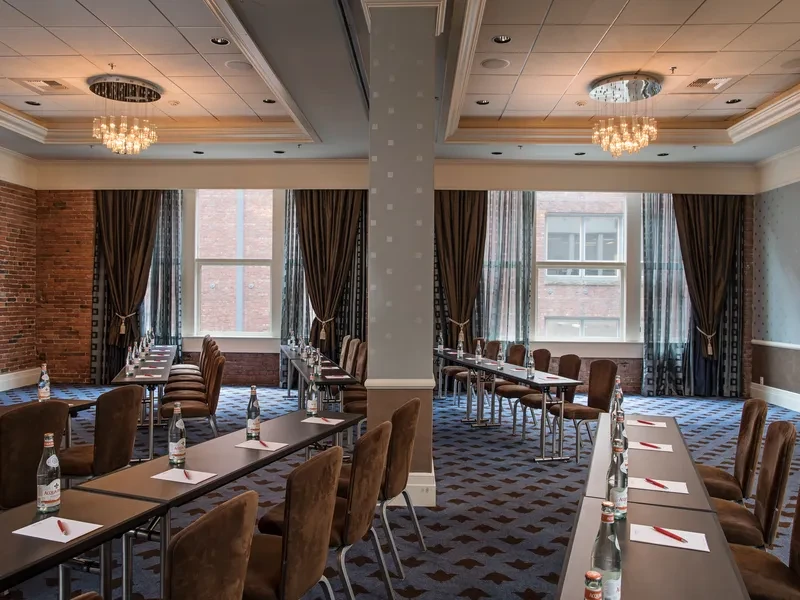 Empty conference room with tables, chairs, a brick wall, and chandeliers.