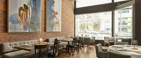 Modern restaurant interior with exposed brick, art, bench, and urban view.