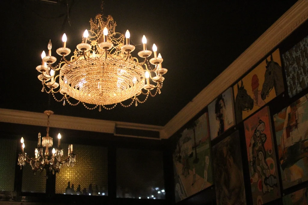 Bright crystal chandeliers illuminate a dark interior with framed artwork.