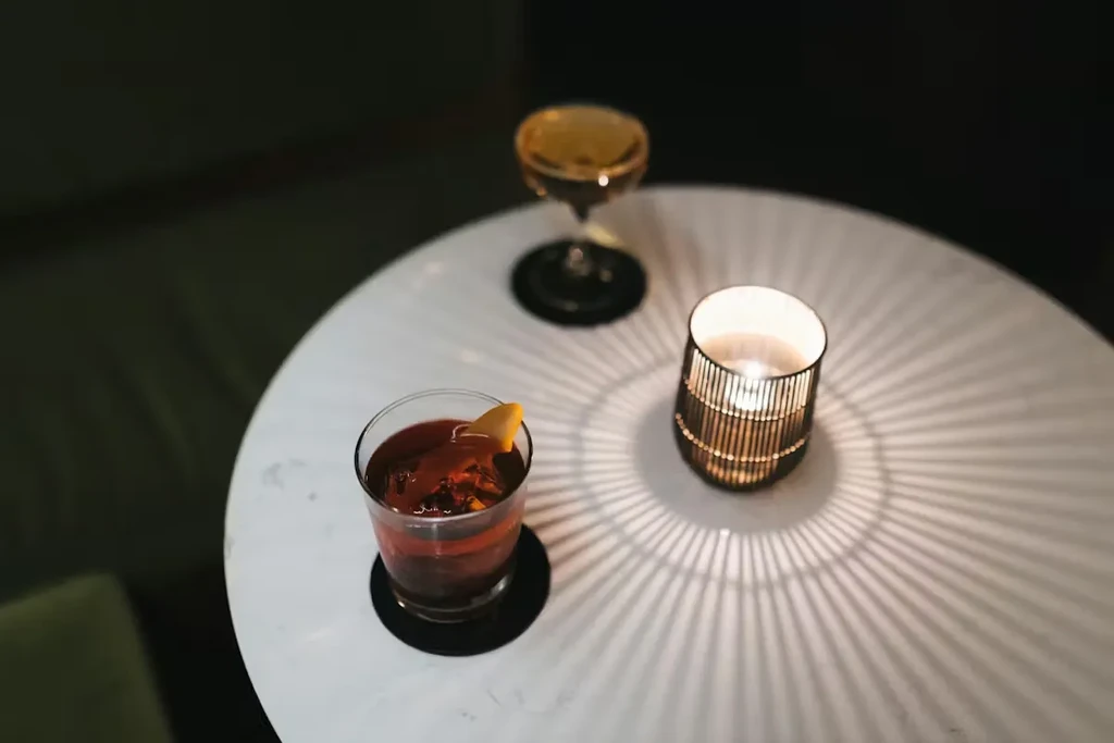 Two cocktails and a glowing candle on a round marble table.