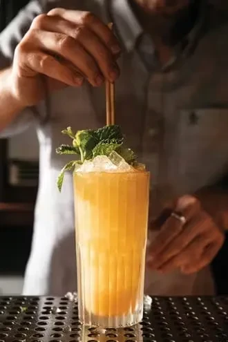 Orange cocktail with crushed ice and mint, a straw being inserted.