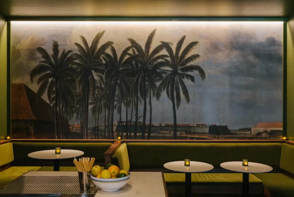 Restaurant interior with large tropical mural, olive seating, and citrus fruits.