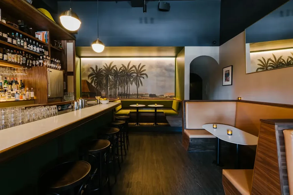Empty, stylish bar with booths, warm lighting, and tropical mural.