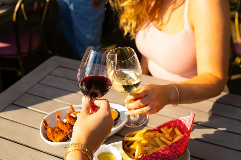 Two people toasting wine glasses with shrimp and fries on a sunny patio.