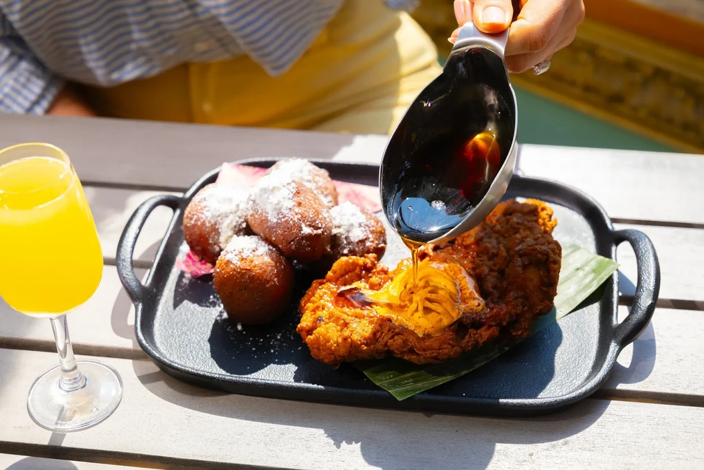 Overhead shot: Hand pours syrup onto fried chicken and fritters.