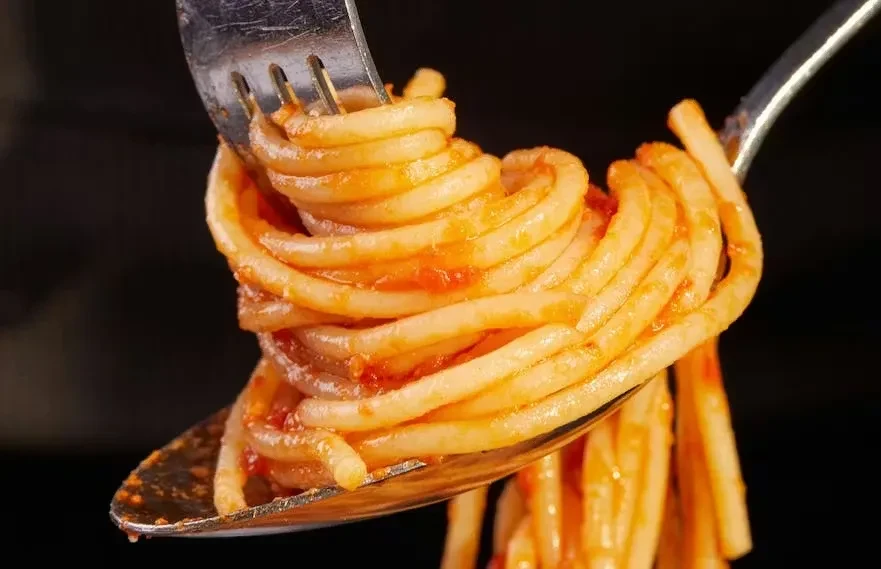 Spaghetti with tomato sauce lifted by a fork and spoon.