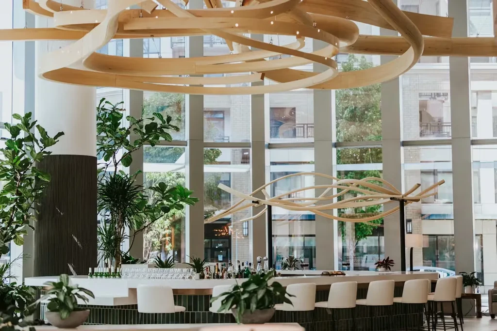 Bright, upscale bar with white counter, green plants, and unique chandelier.