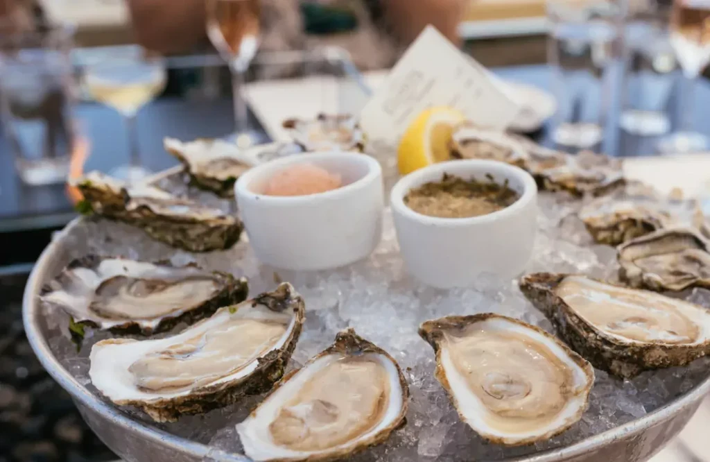 Platter of fresh shucked oysters on ice with lemon and sauces.