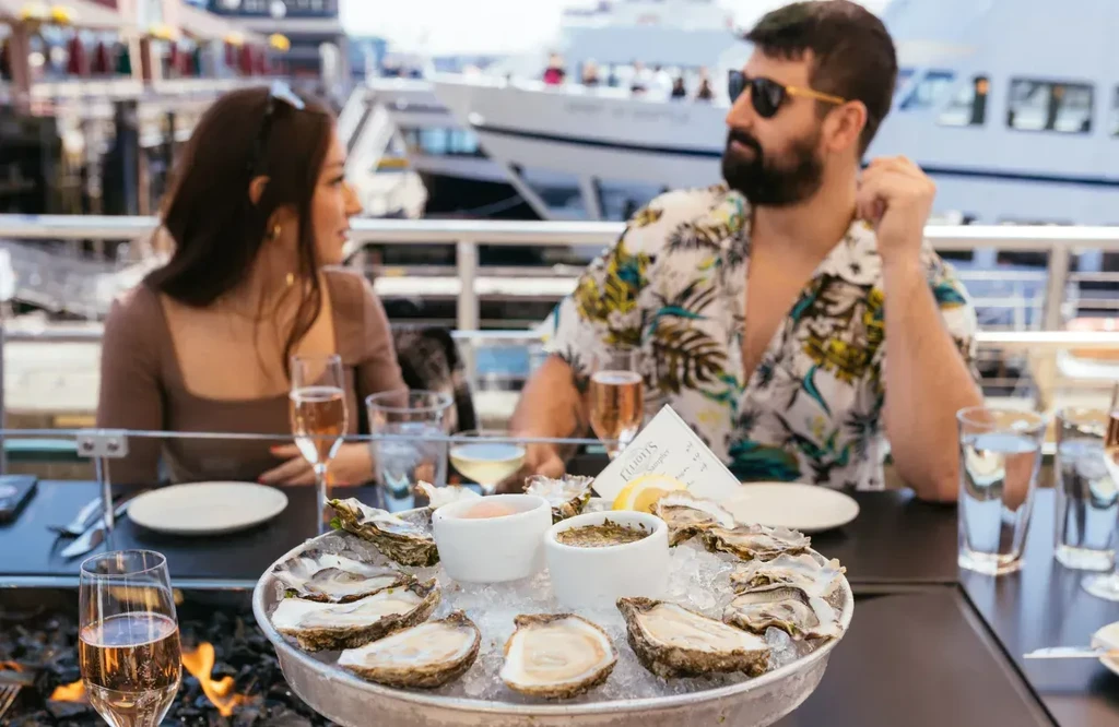 Fresh oysters on ice at a waterfront restaurant fire pit table.
