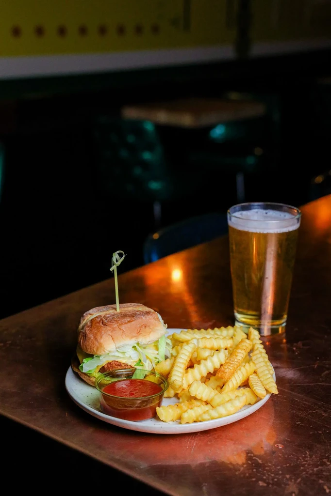 A burger, crinkle-cut fries, ketchup, and beer on a reflective counter.