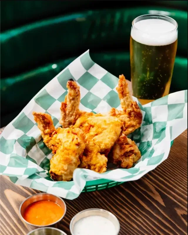 Basket of crispy fried chicken wings, a beer, and two dipping sauces.