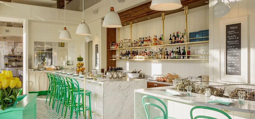 Well-stocked modern bar with marble counter, green stools, and oysters.