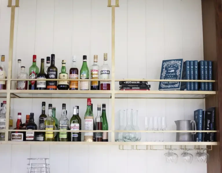 Brass-framed bar shelves stocked with liquor bottles, glassware, and hanging stemware.