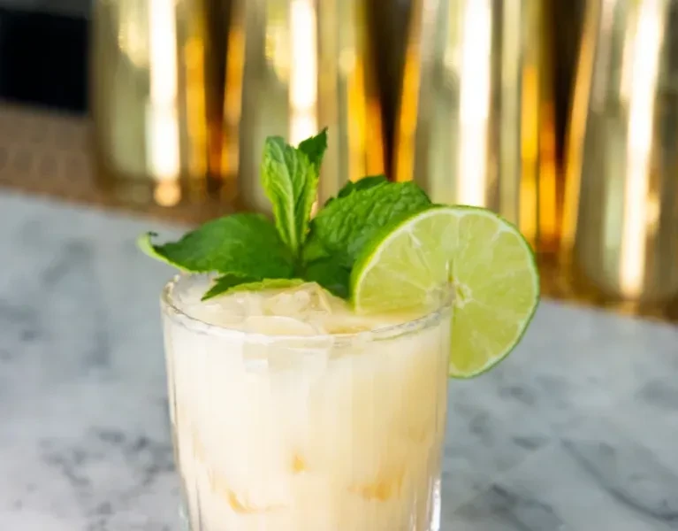 Pale yellow drink in highball glass with lime and mint on marble.