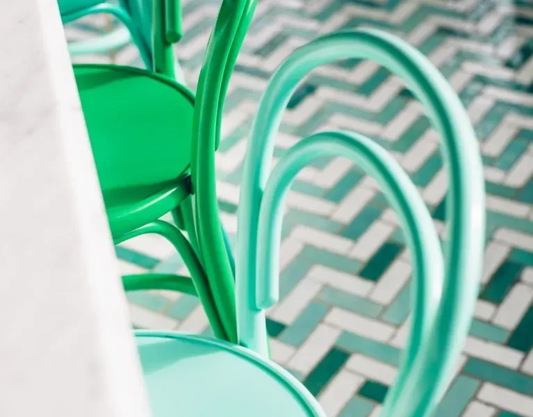 Two green and teal bentwood chairs on a patterned tiled floor.