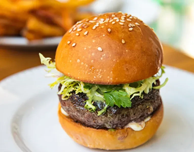 Hamburger with lettuce, sauce, and sesame bun on a white plate.