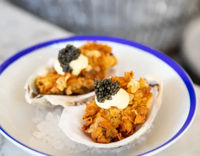 Two crispy fried oysters with sauce, caviar, on crushed ice.