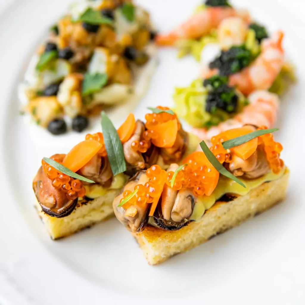 Close-up of toast topped with mussels, salmon roe, and herbs.