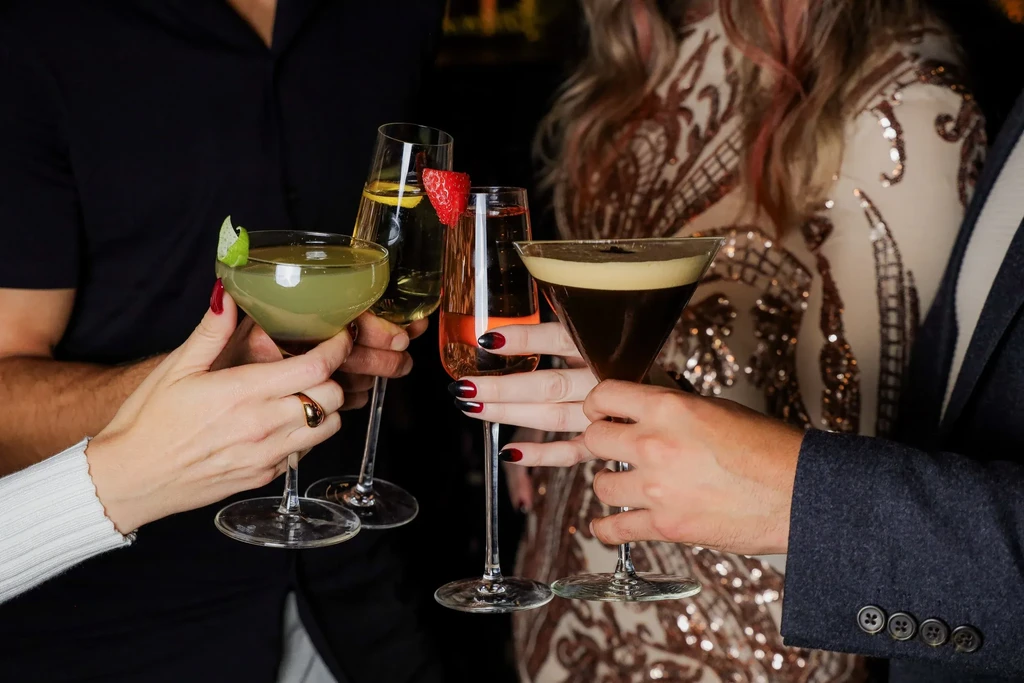 Four hands clinking diverse alcoholic beverages together.