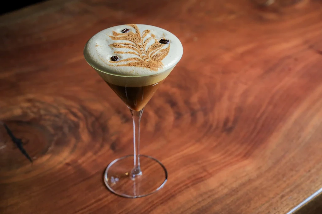 Martini glass cocktail with foam leaf art and three coffee beans.