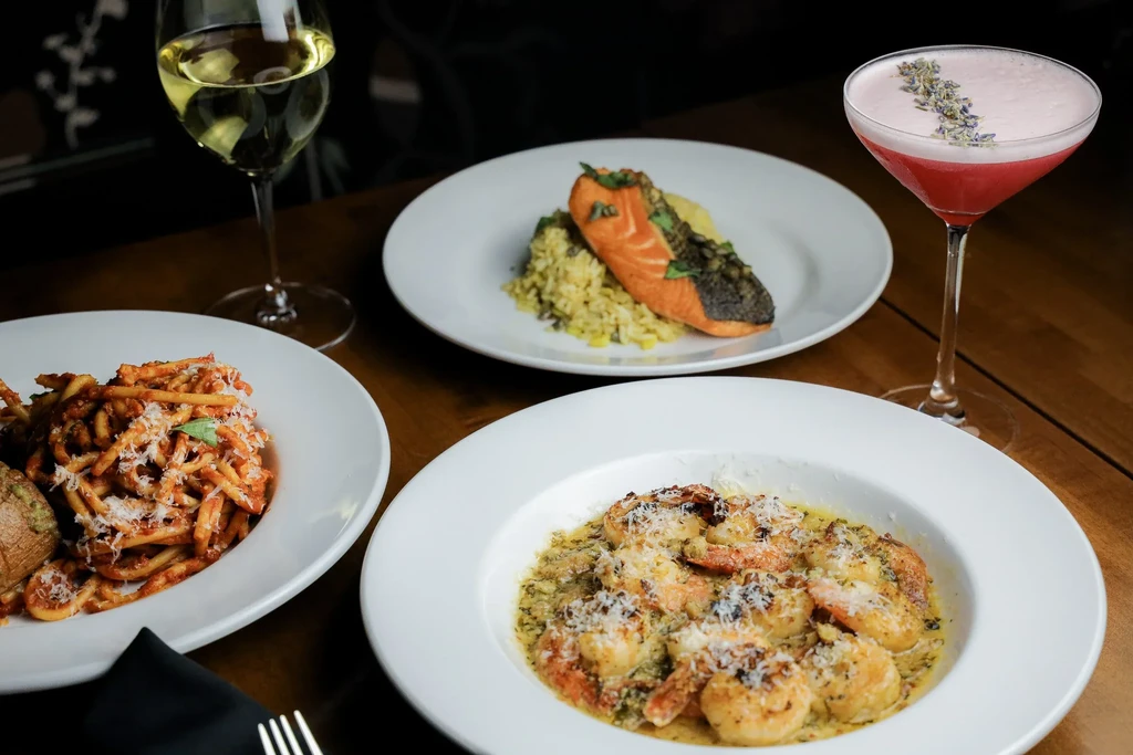 Elegant table with gourmet salmon, pasta, shrimp, wine, and cocktail.