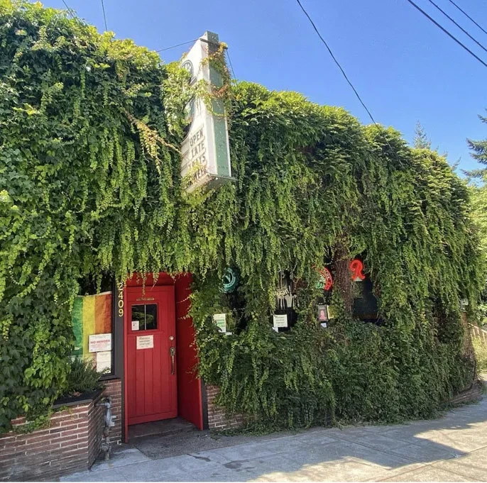 Green ivy-covered restaurant with red door and 'OPEN LATE' sign.