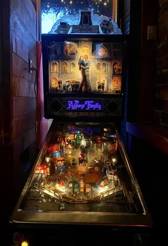 Illuminated "Addams Family" pinball machine with colorful playfield in dim interior.