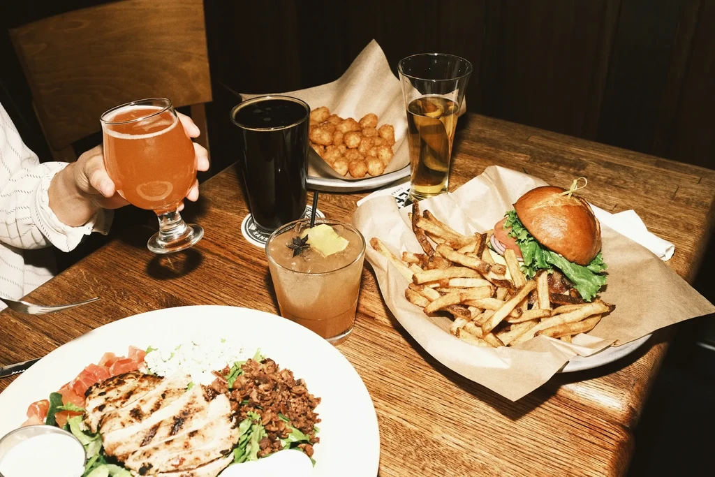 Tabletop scene with grilled chicken salad, burger, fries, and several drinks.