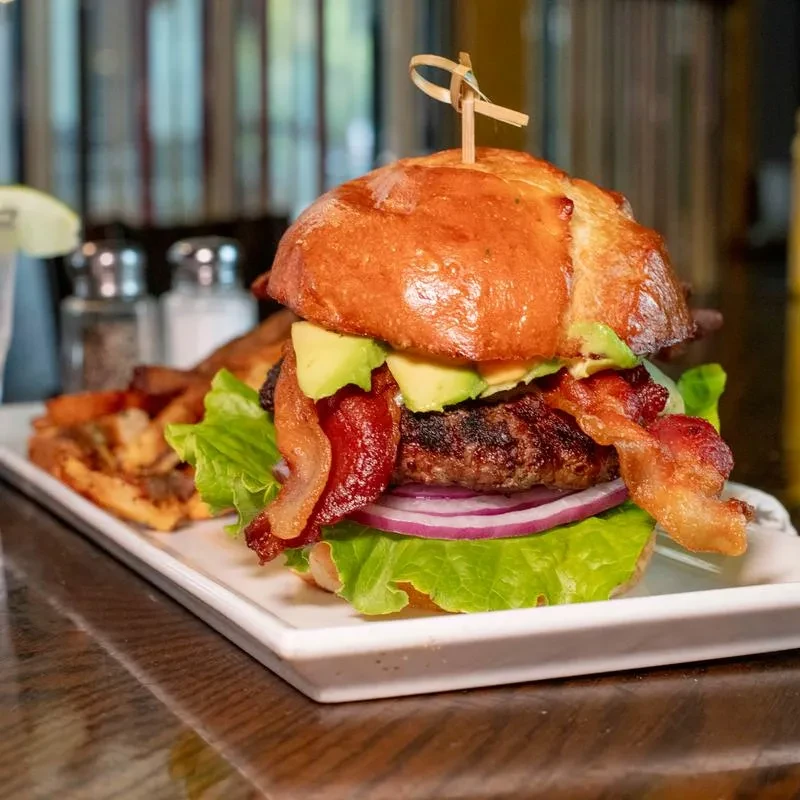 Close-up of a gourmet burger with bacon, avocado, and fries.