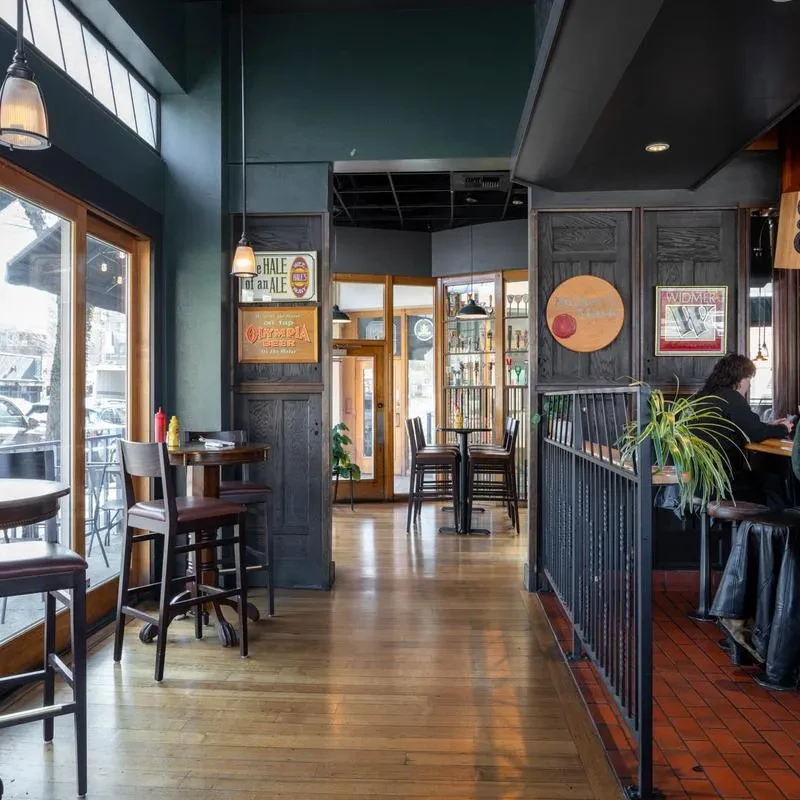 Restaurant interior with dark teal walls, a bar, windows, and vintage signs.