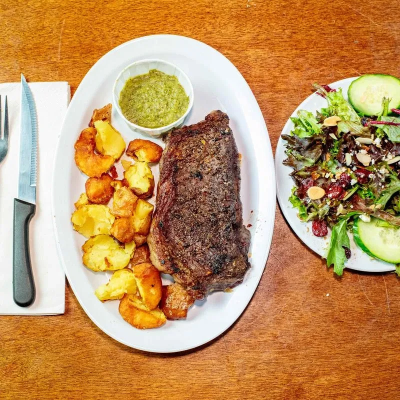 Grilled steak, potato wedges, green sauce, and fresh salad meal.