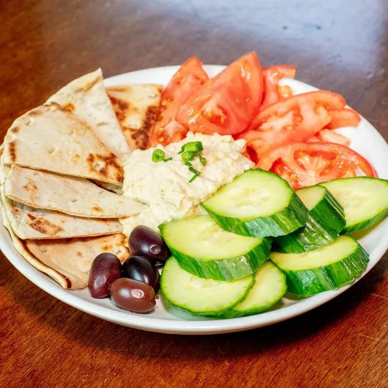 Appetizer platter with hummus, pita bread, tomatoes, cucumber, and olives.