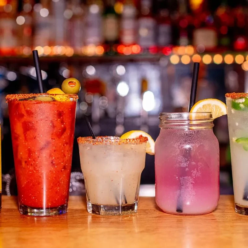 Close-up of four colorful cocktails with salted rims on a bar.