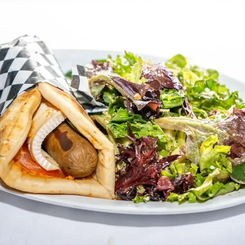 A pita wrap with sausage, onions, sauce, and a mixed green salad.