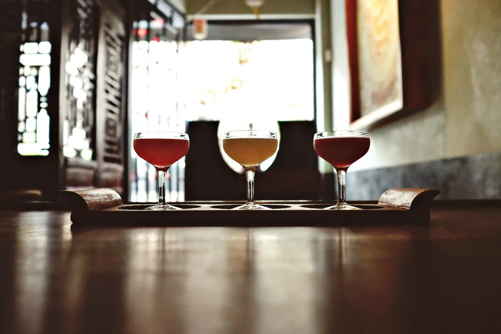 Two red and one yellow cocktail in coupette glasses on a dark tray.