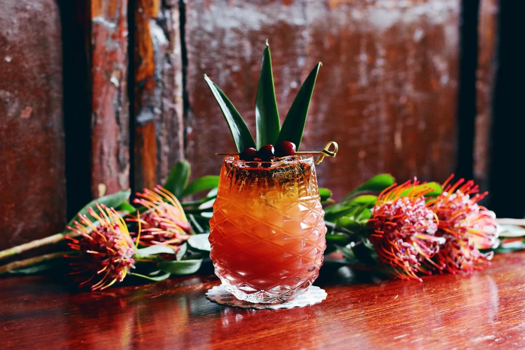 Colorful cocktail in pineapple glass with berries, leaves, and protea.