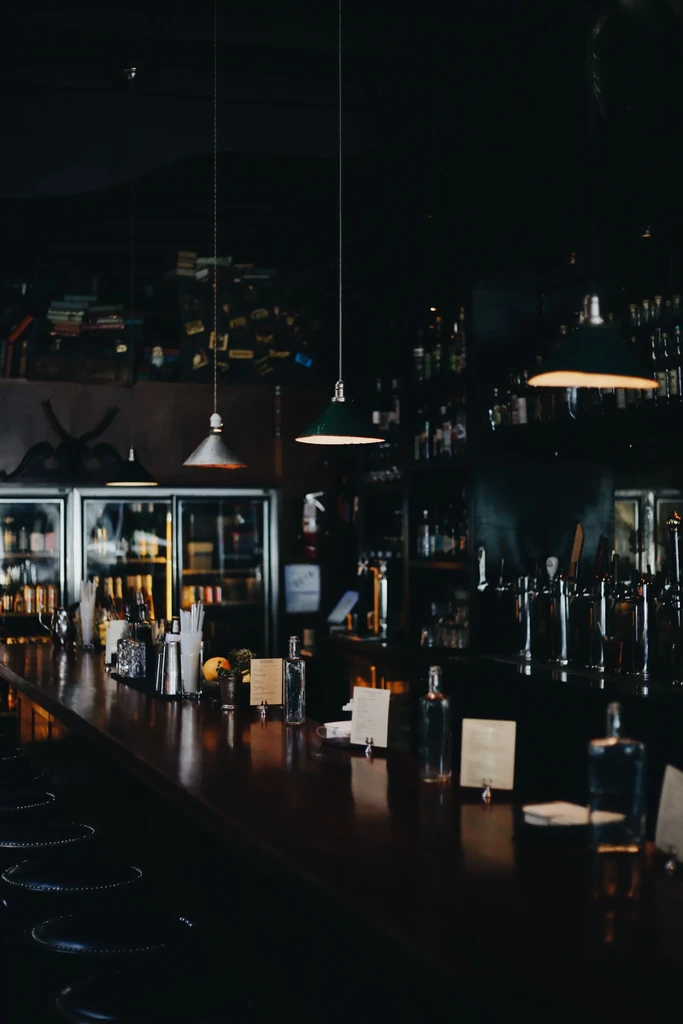 Polished wooden bar counter, stools, liquor bottles, and dim lighting.