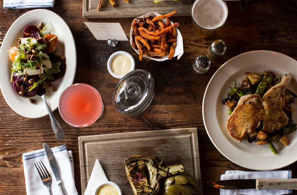 Overhead flat-lay: rustic table with colorful dishes, cocktails, and beer.