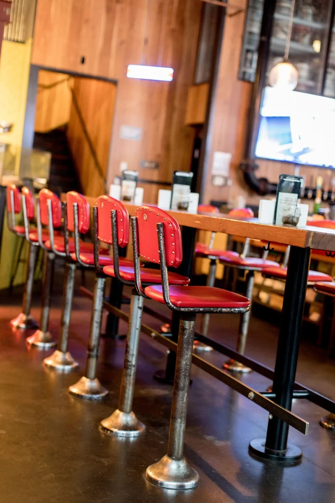Empty red bar stools lined up at a long wooden bar.