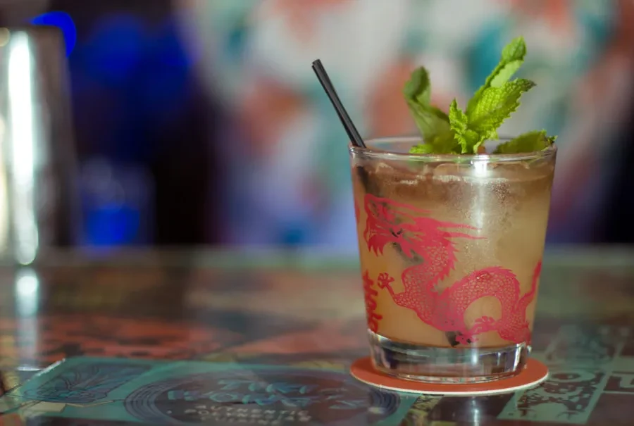 Vibrant cocktail in dragon glass with mint, ice, on patterned table.