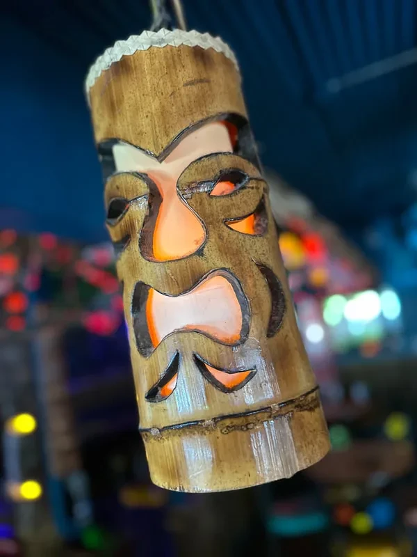Bamboo tiki lantern with a carved face glows warmly amidst blurred lights.