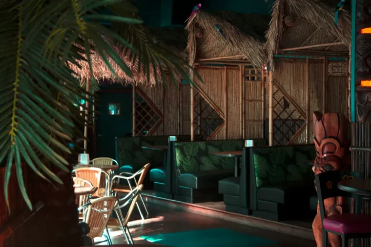 Warm, dim tiki bar interior with bamboo walls and a carved statue.