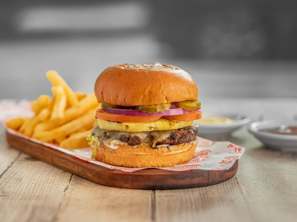 Burger with grilled pineapple, melted cheese, and fries on a wooden board.
