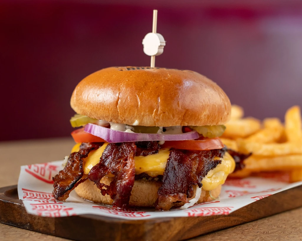 Professionally photographed gourmet bacon cheeseburger with fries on a wooden board.