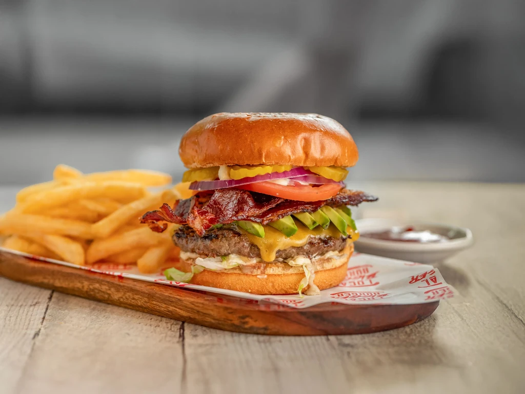 Gourmet burger with fries, avocado, bacon, cheese, served on wood.