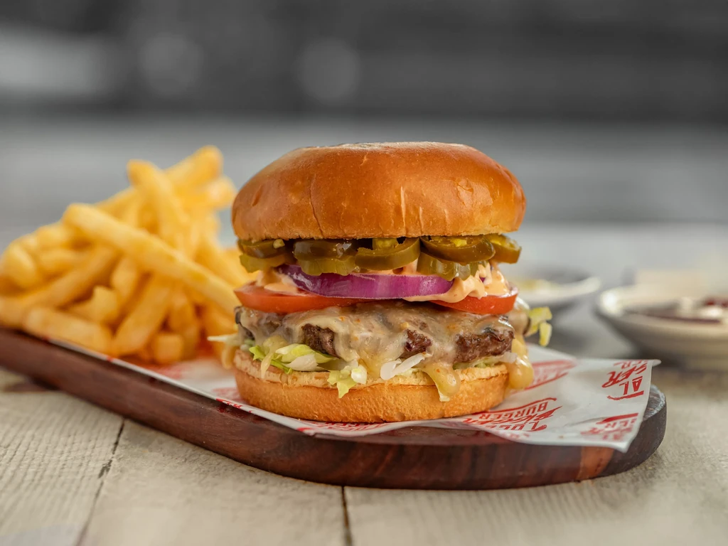 Stacked gourmet burger with melted cheese, jalapeños, and french fries.