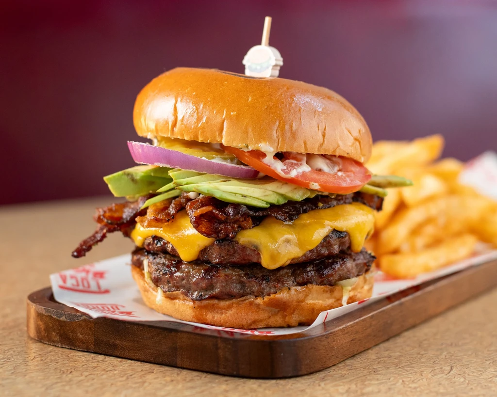 Stacked gourmet burger with cheese, bacon, avocado, and crinkle-cut fries.