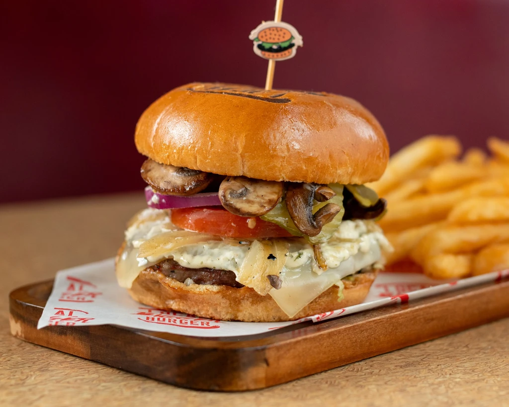 Close-up gourmet burger on a wooden board, with fries and red background.